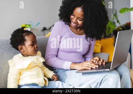 Lächelnde Geschäftsfrau auf Sofa mit Laptop und Tochter, die zu Hause arbeitet Stockfoto