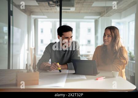 Lächelnde Architekten diskutieren mit Tablet-PC und Bauplänen am Schreibtisch Stockfoto