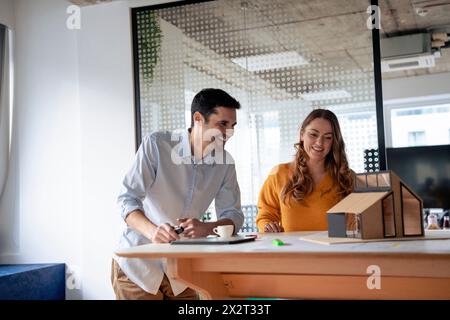 Lächelnde, reife Architekten diskutieren über ein Modell-Zuhause am Schreibtisch Stockfoto