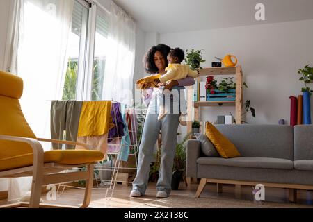 Junge alleinerziehende Mutter mit Tochter, die Kleidung im Wohnzimmer zu Hause trocknet Stockfoto