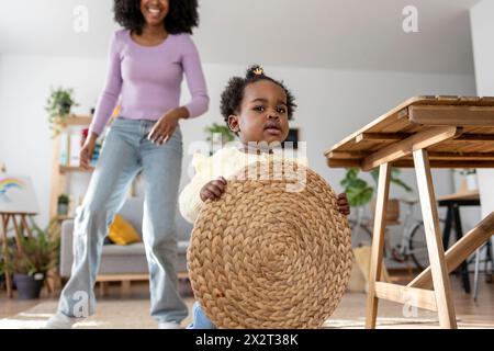 Niedliches Baby Mädchen mit kreisförmiger Platzmatte mit Mutter im Hintergrund zu Hause Stockfoto