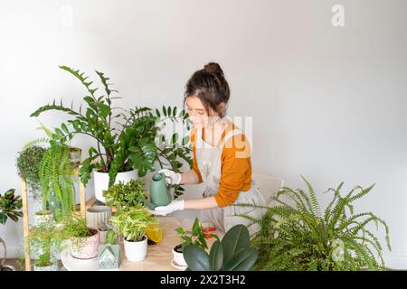 Frau, die Pflanzen auf einem Tisch in der Nähe der Wand im Kinderzimmer tränkt Stockfoto