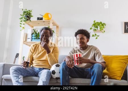 Glücklicher Senior Mann und Enkel, der zuhause das Spiel zusieht Stockfoto