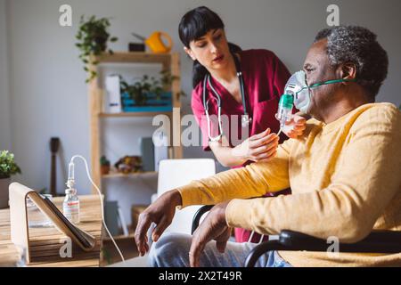 Pflegende, die zu Hause im Rollstuhl sitzende Seniorin mit Sauerstoffmaske bekleidet Stockfoto