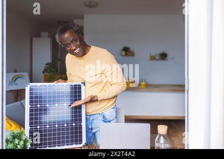 Lächelnder Seniorenmann, der Solarpanel zu Hause zeigt Stockfoto