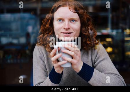 Ein lächelnder Mann hält eine Kaffeetasse im Café Stockfoto