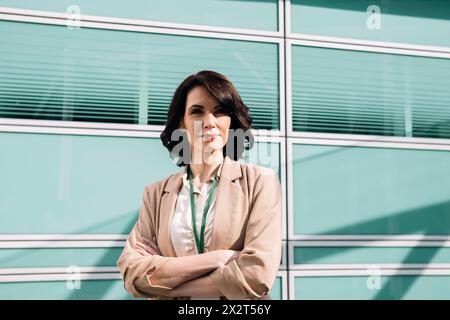 Selbstbewusste Geschäftsfrau, die einen Blazer trägt und die Arme überkreuzt Stockfoto