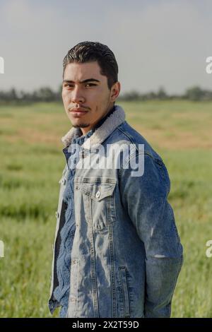 Selbstbewusster junger Mann in Jeansjacke, der auf der Wiese steht Stockfoto