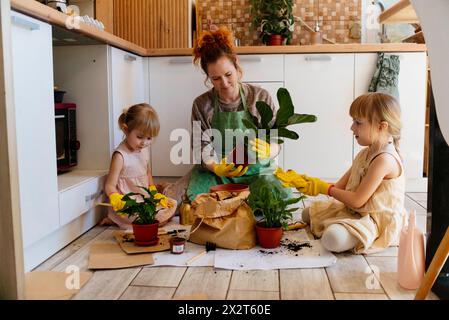 Mutter, die eine Topfpflanze mit Töchtern zu Hause in der Küche sitzt Stockfoto