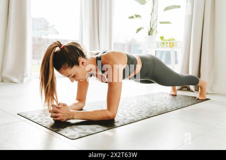 Entschlossene Woman-Plank-Position auf Yogamatte zu Hause Stockfoto