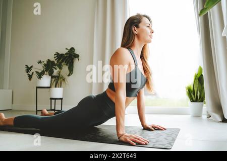 Frau übt zu Hause Cobra auf Yogamatte Stockfoto