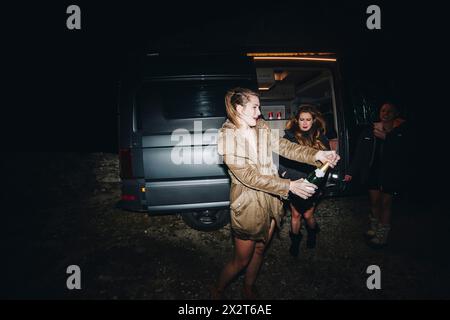 Frau, die nachts Champagner öffnet, feiert Silvester mit Freunden in der Nähe des Wohnmobils Stockfoto