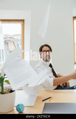 Frustrierter Geschäftsmann, der Dokumente am Schreibtisch im Büro wirft Stockfoto