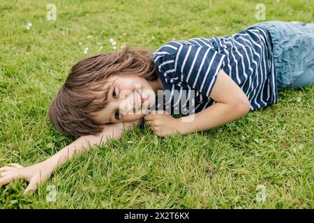 Glücklicher Junge in gestreiftem T-Shirt, der auf dem Rasen liegt Stockfoto