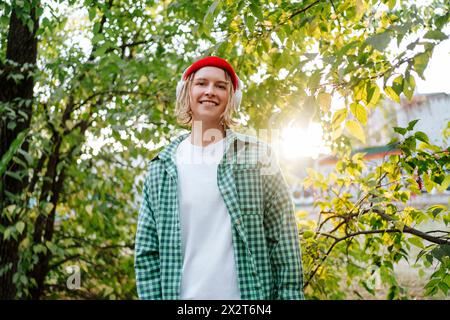 Lächelnde Frau, die Musik über kabellose Kopfhörer hört und vor Bäumen steht Stockfoto