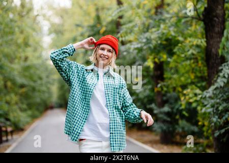 Lächelnde junge Frau mit Strickmütze und kariertem Hemd im Park Stockfoto