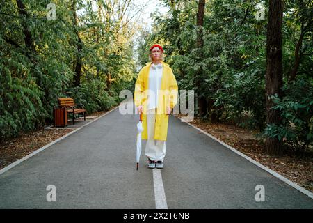 Junge Frau in gelbem Regenmantel und mit Regenschirm auf der Straße Stockfoto