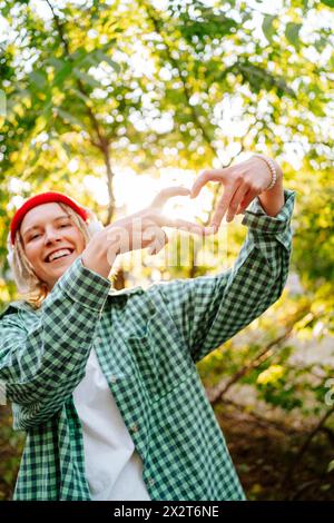 Glückliche junge Frau, die vor Bäumen im Park eine Geste in Herzform drückt Stockfoto