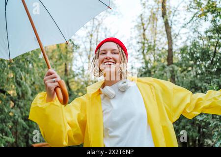 Lächelnde junge Frau mit gelbem Regenmantel und Regenschirm im Park Stockfoto