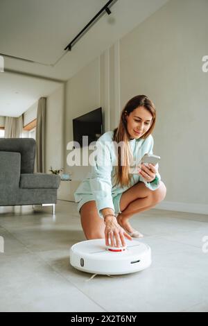 Frau, die zu Hause den Roboter-Staubsauger anschaltet Stockfoto