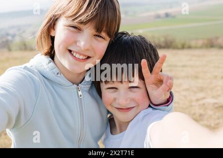 Lächelndes Mädchen, das Friedenszeichen zeigt und Selfie mit Bruder macht Stockfoto