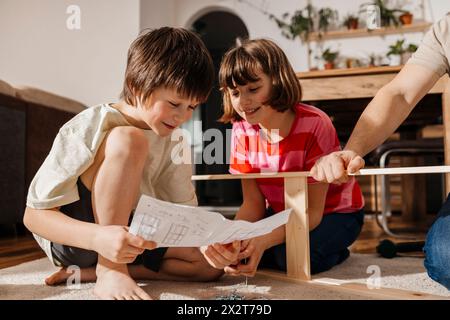 Geschwister lesen die Bedienungsanleitung des Vaters, der Möbel zu Hause zusammenbaut Stockfoto