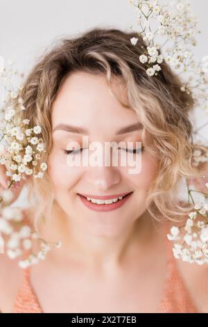 Lächelnde Frau mit gypsophila-Blüten auf blonden lockigen Haaren Stockfoto