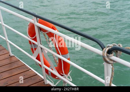 Eine orange Schwimmweste auf dem Geländer eines Bootes auf dem Wasser Stockfoto