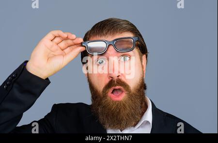 Nahaufnahme Porträt des aufgeregten, erstaunten, schockierten Mannes nimmt die Brille ab. Staunender bärtiger Mann im Anzug, der seine Brille abzieht. Ein überraschter Geschäftsmann Stockfoto