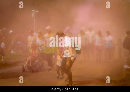 Ein junges Mädchen im Rollstuhl mit anderen Familien rennt durch den Nebel des farbigen Pulvers beim Colour Run, zu Hilfe des St. Rocco's Hospice, Warrington Stockfoto