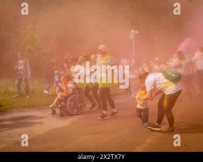 Ein junges Mädchen im Rollstuhl mit anderen Familien rennt durch den Nebel des farbigen Pulvers beim Colour Run, zu Hilfe des St. Rocco's Hospice, Warrington Stockfoto