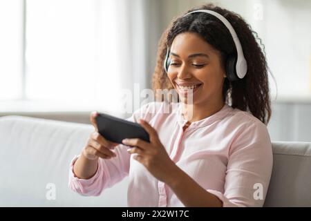 Glückliche Dame mit Kopfhörern, die zu Hause das Telefon benutzen Stockfoto