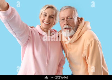 Reifes Paar in Hoodies, das Selfie auf blauem Hintergrund macht Stockfoto