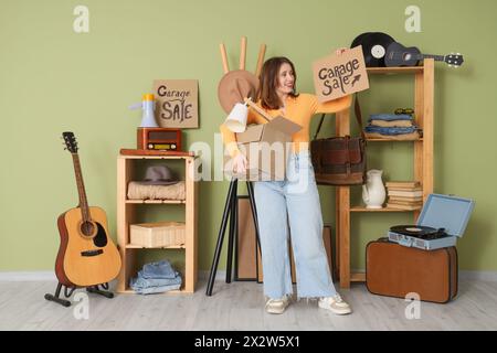 Eine junge Frau, die Pappe mit Text in DER GARAGE hält und im Zimmer mit unerwünschten Sachen Stockfoto