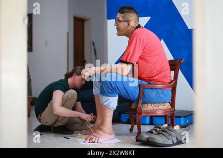 Maracay, Venezuela. April 2024. Adrian Wessels (l) misst den Fuß des venezolanischen Jeison Rodriguez. Rodriguez, dessen Füße mehr als 40 Zentimeter lang sind, wurde vom deutschen Schuhmacher Wessels mit Spezialschuhen versehen. Quelle: Jesus Vargas/dpa/Alamy Live News Stockfoto