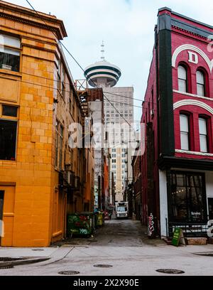 Ein Blick auf die Gasse zwischen zwei farbenfrohen denkmalgeschützten Gebäuden an der Cambie Street in Gastown mit dem Vancouver Lookout Tower, der dahinter aufragt Stockfoto