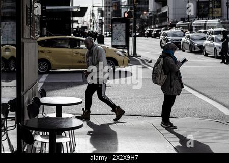 Ein Mann, der an zwei Kaffeetischen an der Kreuzung von Georgia Street und Howe Street vorbeigeht, und eine Frau, die auf ihr Handy blickt. Stockfoto