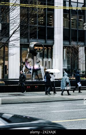 Ein Foto von Menschen, die auf dem Bürgersteig der Burrard Street in Ponchos laufen und Regenschirme vor einem Brunnen halten Stockfoto