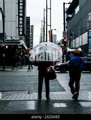 Vancouver, Kanada - 28. Februar 2024: Ein Mann mit einem durchsichtigen Regenschirm und einer Seesack wartet an einem regnerischen Morgen darauf, die Georgia Street zu überqueren Stockfoto