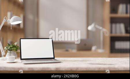 An dem Tisch befinden sich ein Laptop mit weißem Bildschirm, eine Kaffeetasse, eine Tischlampe und eine Einrichtung in einem modernen Büro. Nahaufnahme des Arbeitsbereichs. Stockfoto