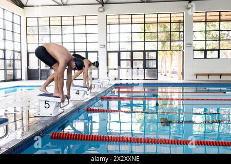 Verschiedene junge Schwimmer, darunter ein männlicher Kaukasier und eine Frau mit birassischer Rasse, die sich auf das Tauchen vorbereiten Stockfoto