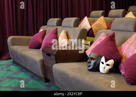 Schwarz-weiße Masken auf weichem Sofa mit Kissen im Kino. Stockfoto