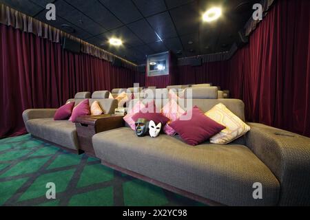 Zwei Masken auf Sofa mit Kissen und Projektor in kleinem Kino. Stockfoto