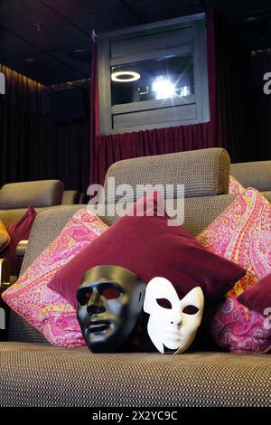 Schwarz-weiße Masken auf Sofa mit Kissen und Projektor im Kino. Stockfoto