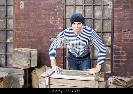 Junger Mann in gestreiften Westenständern, mit den Händen auf eine Holzkiste Stockfoto