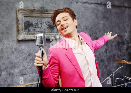 Ein junger Mann in rosa Anzug singt mit geschlossenen Augen ins Mikrofon Stockfoto