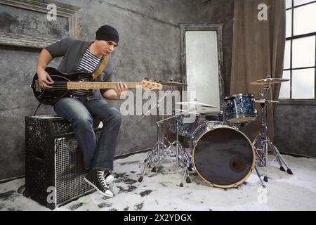 Junger Musiker spielt E-Bass-Gitarre, sitzt auf Verstärker im schneebedeckten Raum Stockfoto