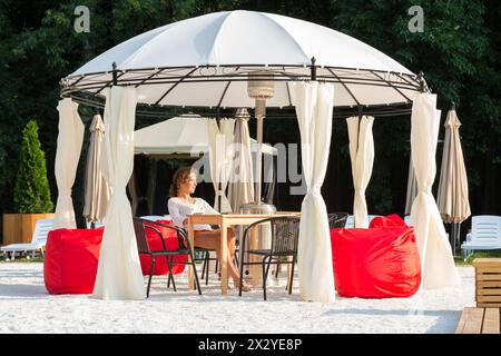 MOSKAU - 28. JUL: Schönes Mädchen in gemütlichem Open-Air-Café mit roten Poufs im BASSEYN in Sokolniki am 28. Juli 2012 in Moskau, Russland. Es ist ein gutes Hotel Stockfoto