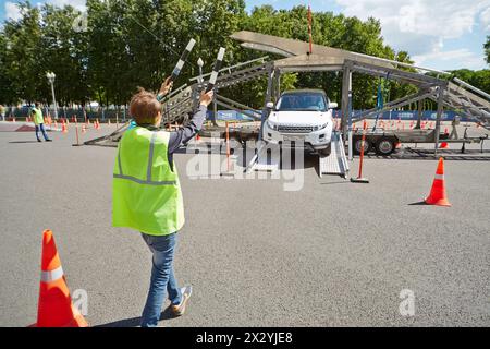 MOSKAU – JUN 30: Junge in Uniform-Jacke mit zwei gestreiften Verkehrsstäben weist das Auto von der Autoplattform auf dem Speedfest in Luschniki, 22. Juni, hinunter. Stockfoto