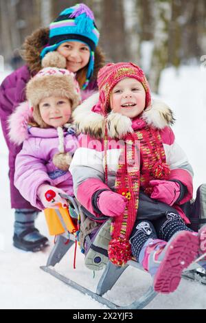 Mädchen schiebt Schlitten mit zwei jüngeren Kindern im Winterpark Stockfoto